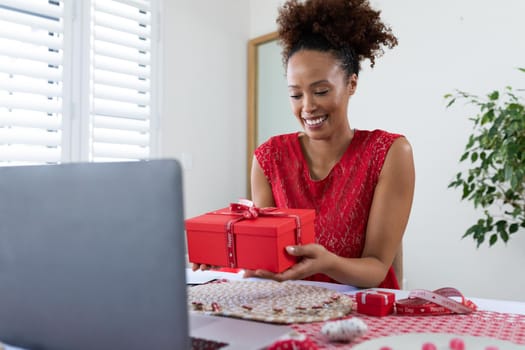 African american woman holding gift box on videocall on laptop at home. distant celebration of valentines day online and dating concept