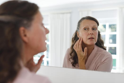 Senior caucasian woman in bathroom, looking at her face in mirror. retirement lifestyle and the aging process.