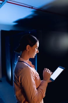 Caucasian female engineer using digital tablet in computer server room. database server management and maintenance concept
