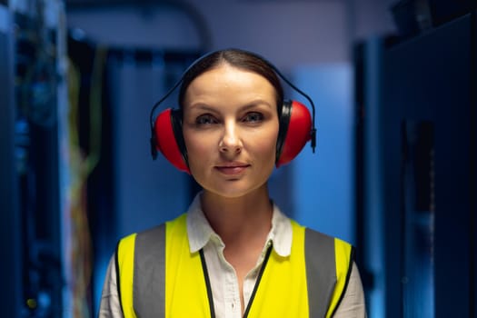 Portrait of caucasian female engineer wearing ear plugs in computer server room. database server management and maintenance concept