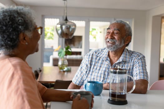 Happy african american senior couple sitting in kitchen with coffee and talking. healthy retirement lifestyle at home.