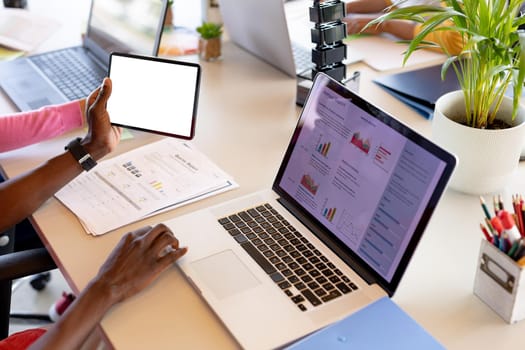 Businessman holding digital tablet with copy space while typing on laptop at desk in office. business, wireless technology, casual and office.