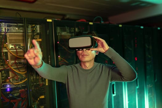 Asian man wearing vr headset touching an invisible screen in computer server room. database server and futuristic technology concept