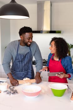 Happy african american couple wearing aprons, baking together and looking at camera. family time, having fun together at home.