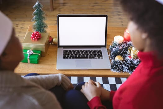 African american adult daughter and mother making christmas laptop video call, copyspace on screen. christmas, festivity and communication technology at home.