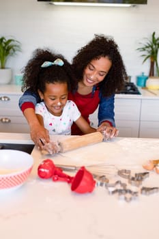 Happy african american mother and daughter baking together in kitchen. family time, having fun together at home.