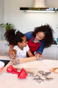 Happy african american mother and daughter baking together in kitchen. family time, having fun together at home.