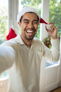 Portrait of happy biracial man in santa hat making christmas video call. christmas, festivity and communication technology.