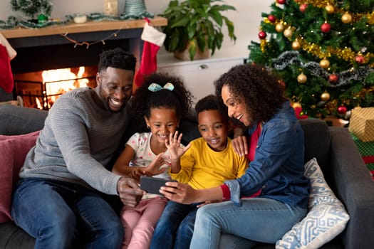 Happy african american family having video call on smartphone, christmas decorations in background. christmas, festivity and communication technology.