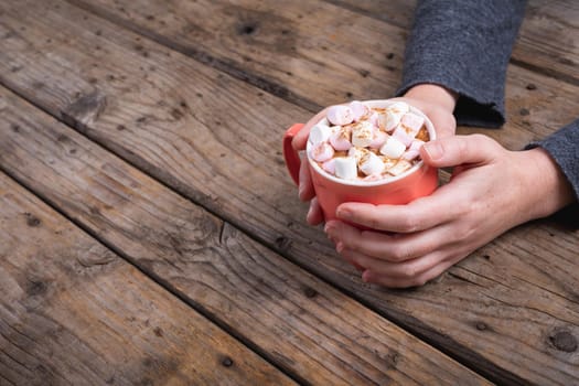 Cropped hands of woman holding mug of hot chocolate drink and marshmallows at table with copy space. lifestyle and cafe culture.