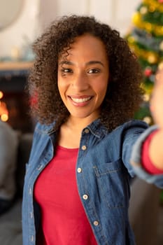 Happy african american woman taking selfie, christmas decorations in background. christmas time and festivity at home.
