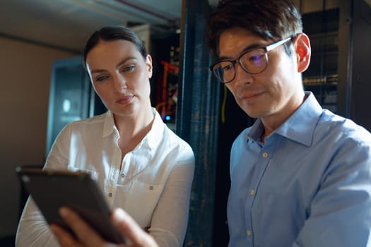 Diverse male and female engineers using digital tablet in computer server room. database server management and maintenance concept
