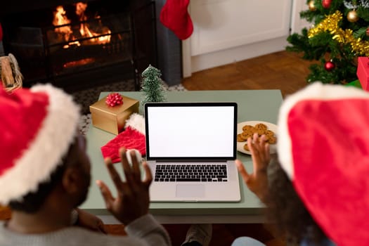 Back view of african american couple wearing santa hats, using laptop with copy space on screen. christmas, festivity and communication technology.