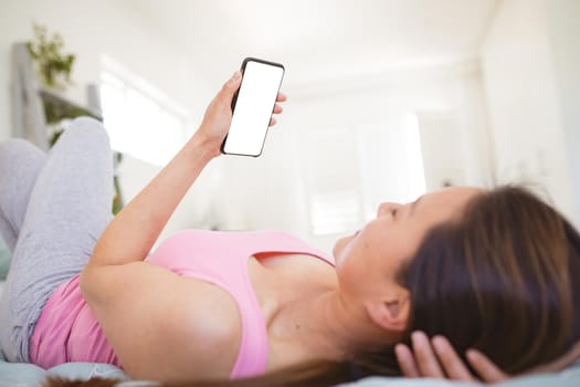 Asian woman lying on bed, using smartphone with copy space on screen. relaxing at home with technology.