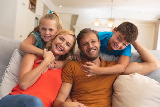 Portrait of caucasian couple with daughter and son sitting on couch and smiling at home. family enjoying quality free time together.