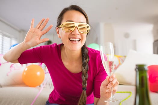 Happy asian woman raising champagne glass making new year's eve laptop video call. celebrating at home with communication technology.