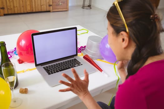 Happy asian woman making new year's eve video call on laptop with copy space on screen. o celebrating at home with communication technology.