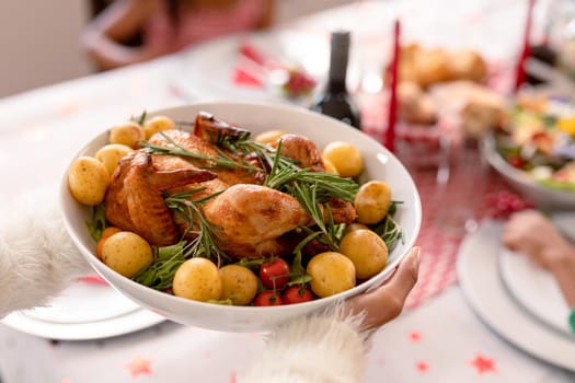 Hand of african american woman holding bowl with chicken and potatoes dish. christmas, festivity and tradition at home.