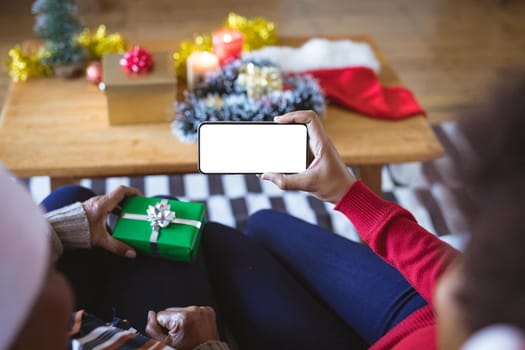 African american adult daughter and mother on christmas smartphone video call, copyspace on screen. christmas, festivity and communication technology at home.