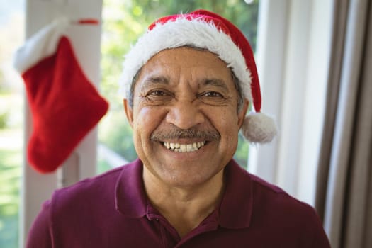 Portrait of happy biracial senior man in santa hat at christmas. christmas, festivity and communication technology.