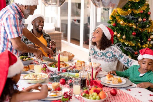 Happy african american multi generation family having christmas meal. family christmas time and festivity together at home.