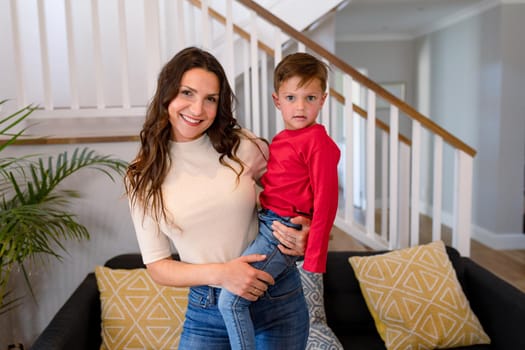 Happy caucasian mother holding son and looking at camera. lifestyle, leisure and spending free time at home.