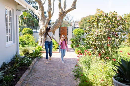 Happy caucasian mother and daughter walking outside and holding hands. family time, having fun together at home.