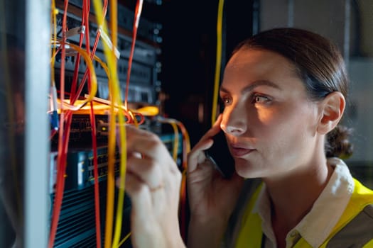 Close up of caucasian female engineer talking on smartphone while inspecting in computer server room. database server management and maintenance concept