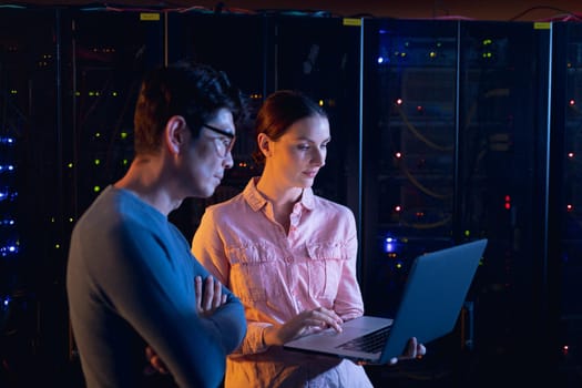 Diverse male and female engineers using laptop in computer server room. database server management and maintenance concept