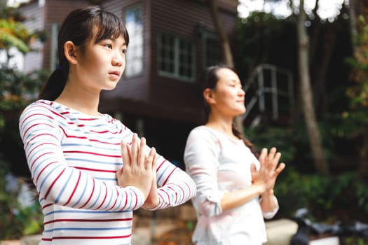 Asian mother and daughter exercising outdoors and practicing tai chi. family fitness time in garden.