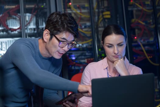 Diverse male and female engineers discussing over a laptop in computer server room. database server management and maintenance concept