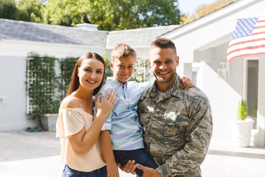 Portrait of caucasian male soldier with son and wife outside house decorated with american flag. soldier returning home to family.