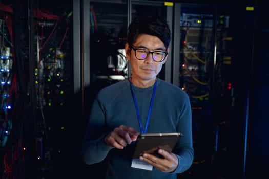 Asian male engineer using digital tablet in computer server room. database server management and maintenance concept