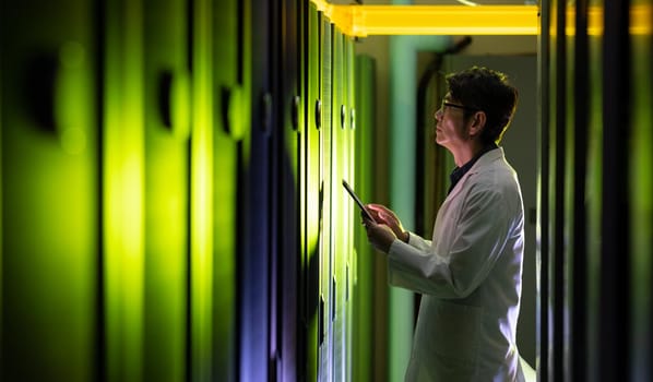 Asian male engineer wearing an apron using digital tablet while inspecting in computer server room. database server management and maintenance concept