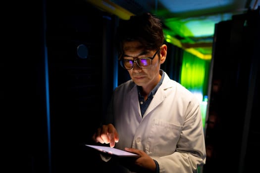 Asian male engineer wearing an apron using digital tablet in computer server room. database server management and maintenance concept