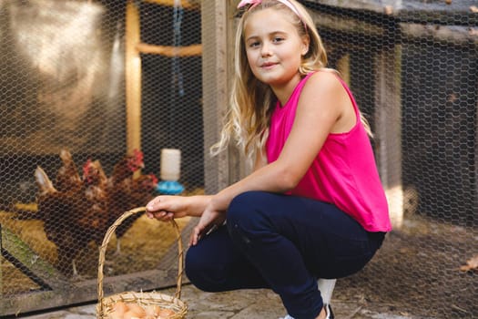 Portrait of smiling caucasian girl collecting eggs from hen house in garden. self sufficiency and spending time at home.