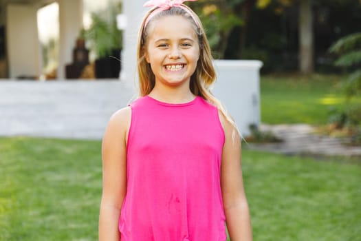 Portrait of smiling caucasian girl outside house looking at camera in garden. spending time at home.