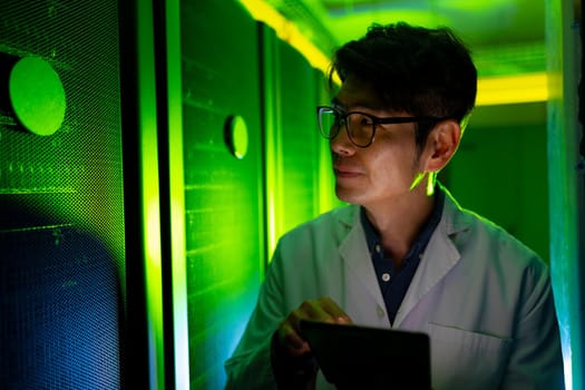 Asian male engineer wearing an apron using digital tablet while inspecting in computer server room. database server management and maintenance concept