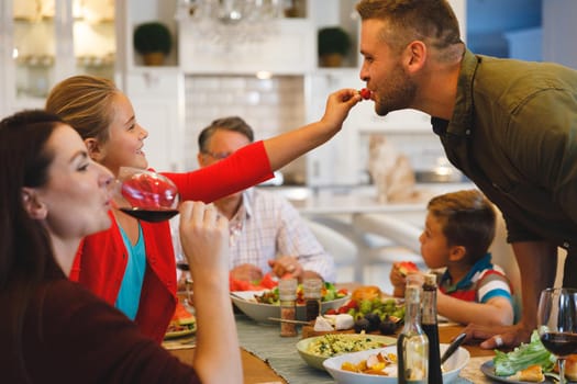 Caucasian daughter feeding father while sitting at table having family dinner. family spending time together at home.