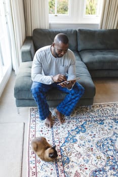 African american man using tablet and sitting on couch in living room. spending time alone at home with technology.