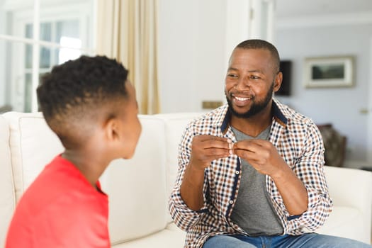 Happy african american father with son sitting on couch in living room talking sign language. father and son communicating without words.