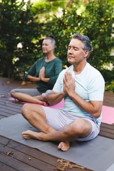 Happy senior caucasian couple practicing yoga, meditating in sunny garden. healthy retirement lifestyle, spending time at home.