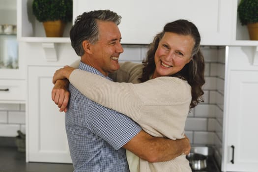Happy senior caucasian couple in modern kitchen, embracing and smiling. retirement lifestyle, spending time at home.