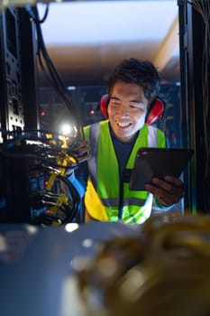Asian male engineer using smartphone flash while inspecting the server in computer server room. database server management and maintenance concept