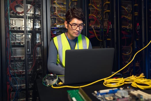 Asian male engineer using a laptop in computer server room. database server management and maintenance concept