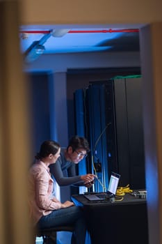 Diverse male and female engineers using smartphone and laptop in computer server room. database server management and maintenance concept