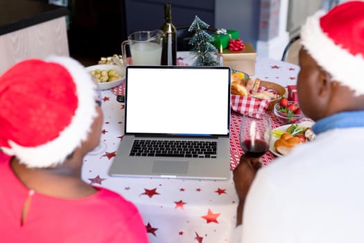 Back view of african american senior couple using laptop with copy space at christmas time. retirement lifestyle, christmas festivities and communication technology.