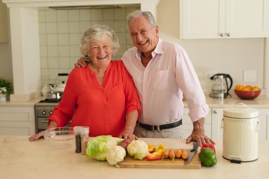 Portrait of senior caucasian couple looking at camera and smiling in kitchen. retreat, retirement and happy senior lifestyle concept.