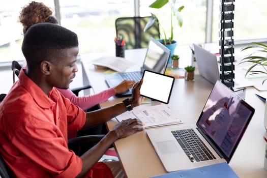 Young african american businessman in casual using digital tablet with copy space at desk in office. business, wireless technology and office.