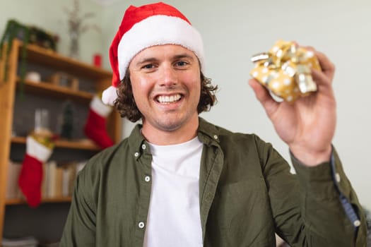 Portrait of caucasian disabled man wearing a santa hat holding christmas gift at home. christmas festivity and celebration concept